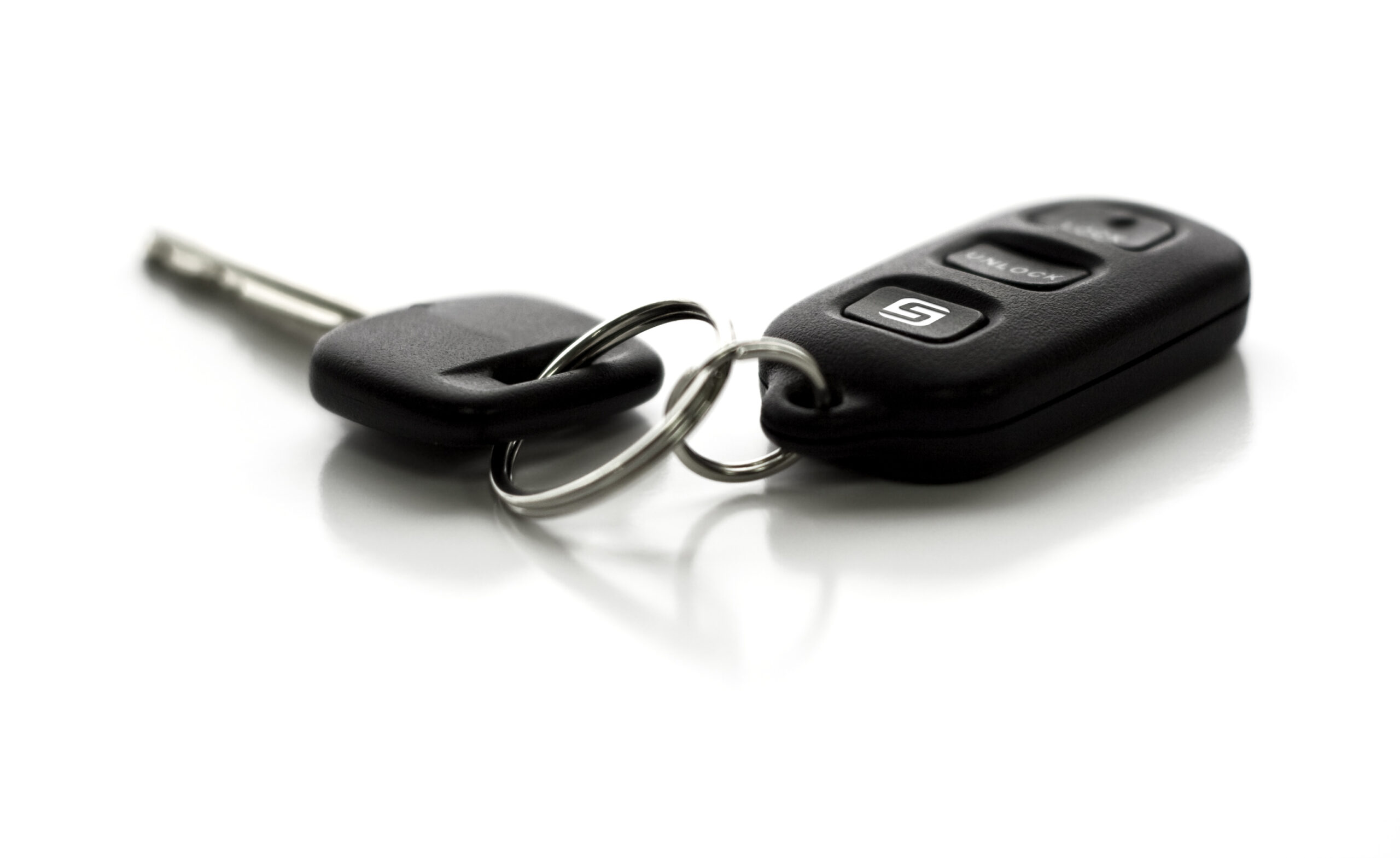 A car key with remote control.  Functions include Lock, Unlock, and Hatch Glass.  Narrow depth of field with focus on closest portion of key and remote.  Isolated on white background.
