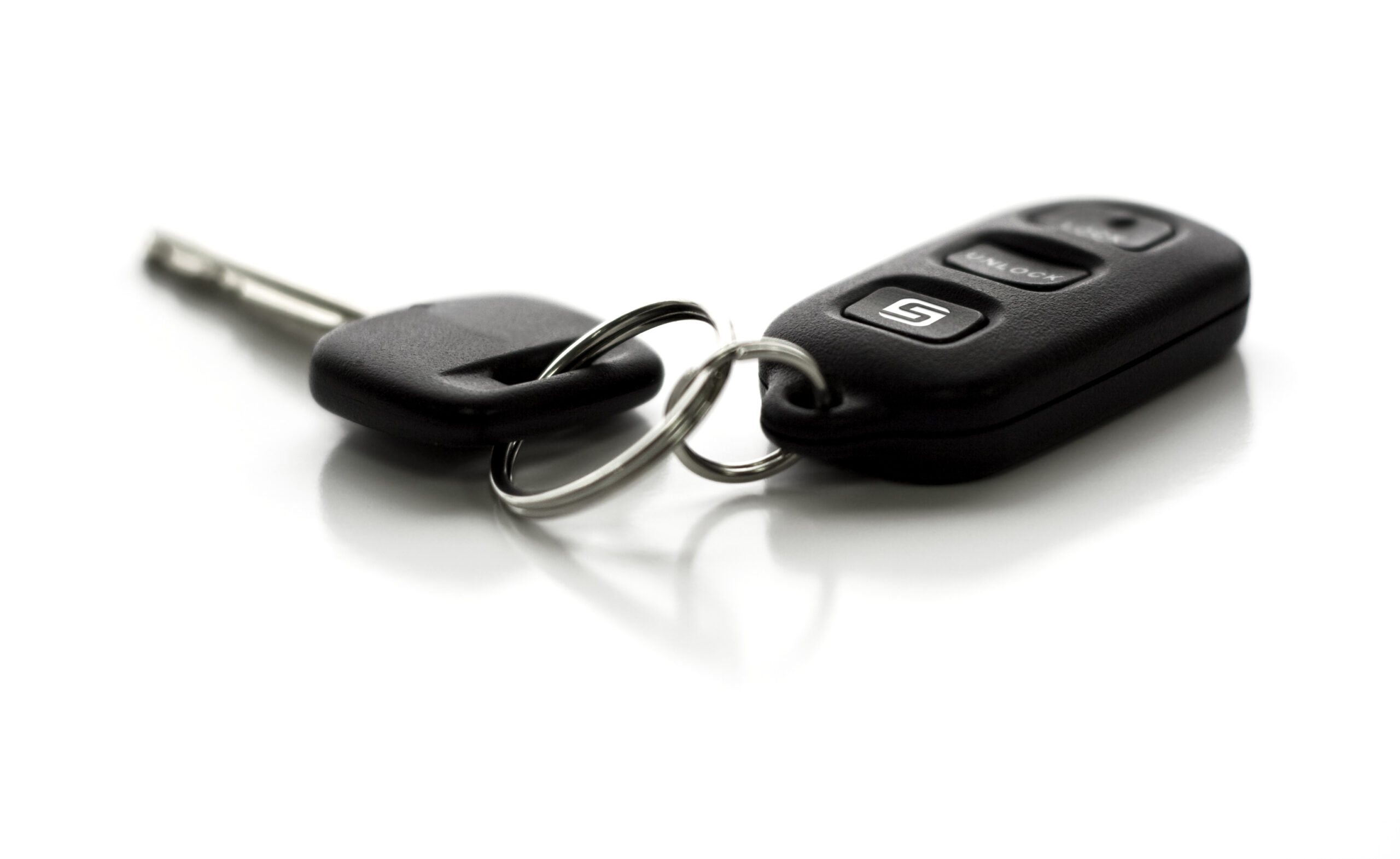 Remote control entry and car key ring on white background A car key with remote control. Functions include Lock, Unlock, and Hatch Glass. Narrow depth of field with focus on closest portion of key and remote. Isolated on white background.